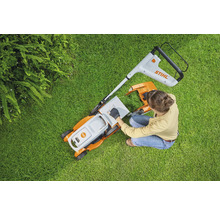 Femeie pregătește mașina de tuns iarba pe gazon. Logo Stihl.