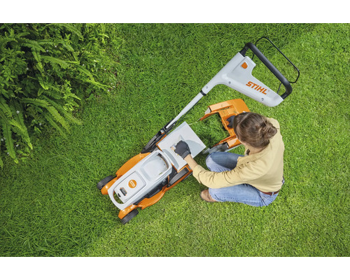 Femeie pregătește mașina de tuns iarba pe gazon. Logo Stihl.