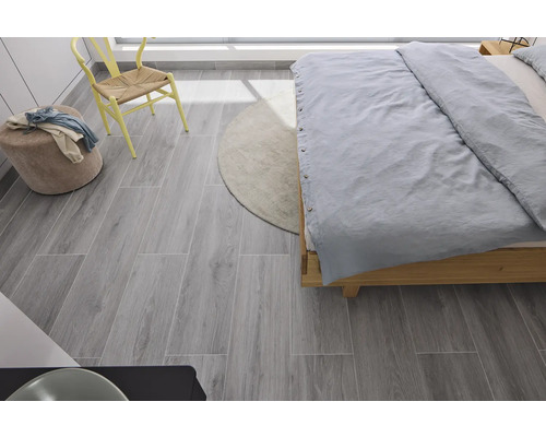 Dormitor cu pat, scaun, taburet, covor și gresie gri cu aspect de lemn