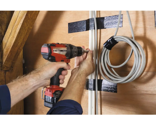 O persoană fixează o conductă pe un perete cu o șurubelniță fără fir. O conductă înfășurată este fixată cu bandă adezivă.