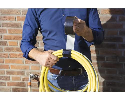 O persoană ține un furtun de grădină galben înfășurat cu bandă adezivă neagră și o rolă de bandă adezivă.