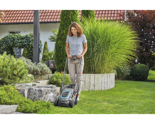 Femeie folosește mașina de tuns iarba în grădină.
