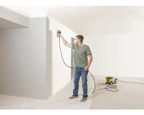 Un bărbat vopsește un perete cu un sistem de pulverizare a vopselei într-o cameră luminoasă