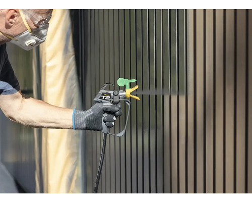 Persoană vopsește gard cu pistol de vopsit