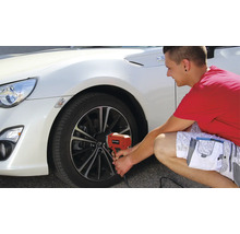 Un bărbat schimbă o anvelopă la o mașină albă cu o cheie de impact electrică.