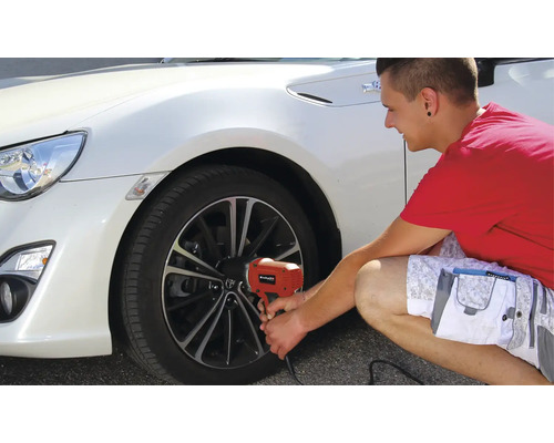Un bărbat schimbă o anvelopă la o mașină albă cu o cheie de impact electrică.