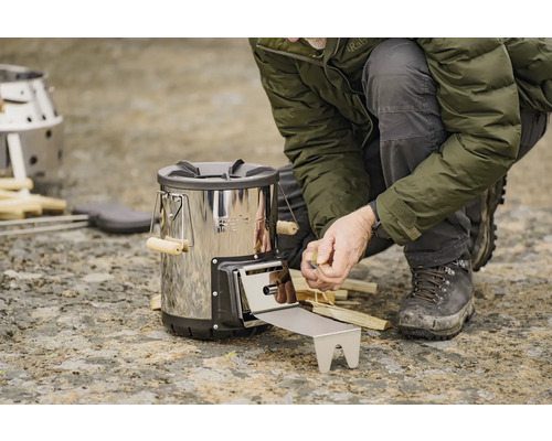 O persoană umple un aragaz hobo cu lemne.