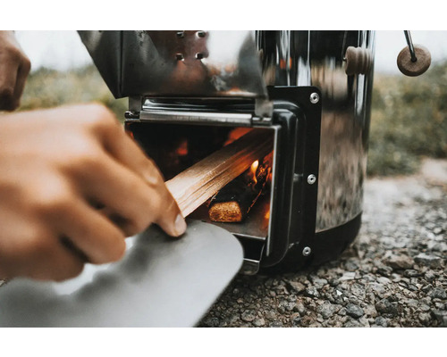 Persoană care pune lemne într-un aragaz portabil de camping.