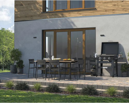 Terasa cu grătar, masă de grădină și scaune de grădină în fața unui perete de casă