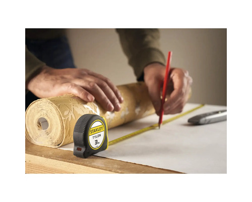 O persoană măsoară o rolă de tapet cu o bandă de măsurat și o marchează cu un creion.