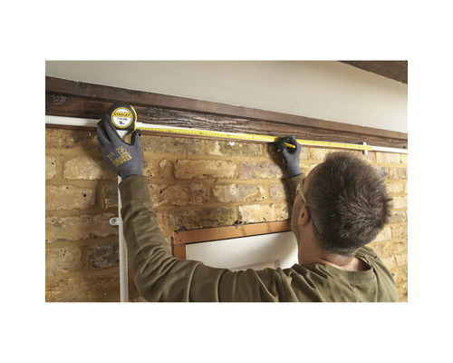 O persoană măsoară lungimea unui perete cu o bandă de măsurare.