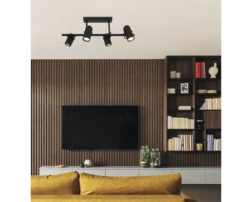 Cameră de zi cu plafonieră neagră cu patru spoturi, televizor și bibliotecă.