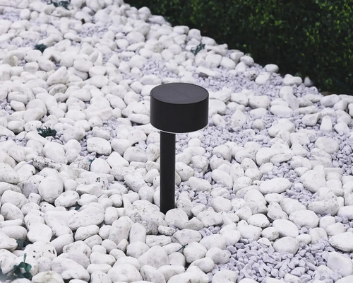 Lampa solară neagră în grădină printre pietre albe