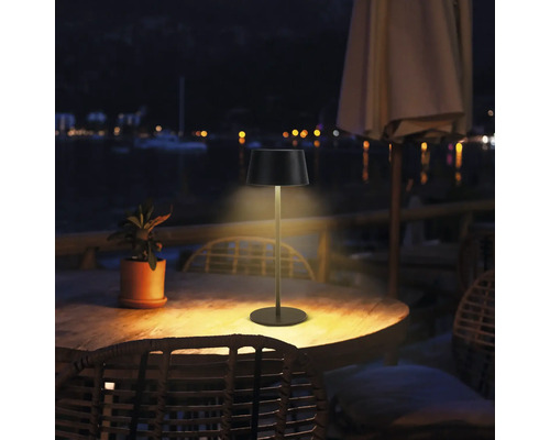 Fotografie de exterior a unei lămpi de masă pe o masă de lemn afară noaptea.