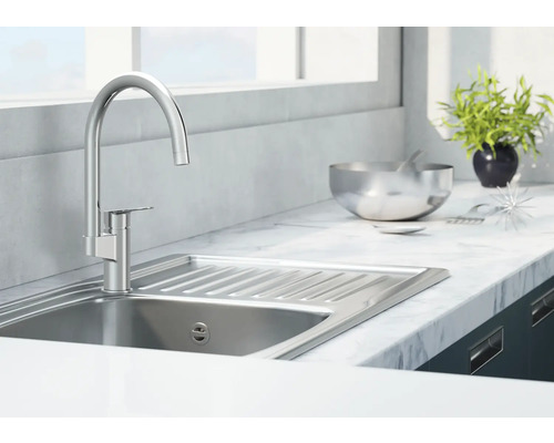 Chiuvetă din oțel inoxidabil cu robinet într-o bucătărie luminoasă.