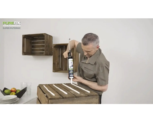 Un bărbat aplică adeziv pe o ladă de lemn pentru a fixa lăzi de lemn pe perete