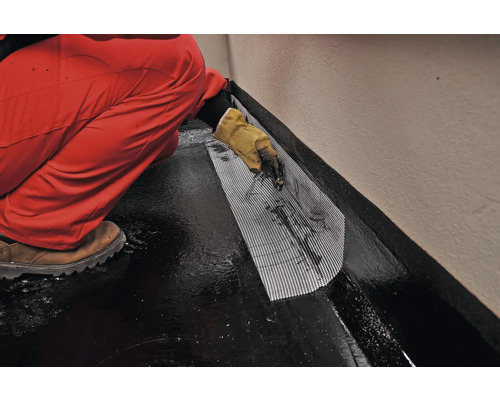 O persoană aplică un strat de etanșare cu bandă textilă pe o podea.