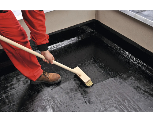 Aplicarea hidroizolației bituminoase pe o terasă pe acoperiș cu o pensulă plată.