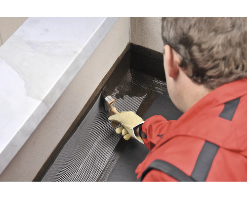 O persoană aplică un material de etanșare pe o țesătură cu o pensulă