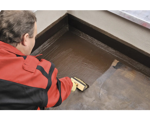 Mester aplică etanșant cu o perie pe podea