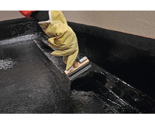 Aplicarea unui strat bituminos gros cu o gletieră de către o persoană cu mănuși