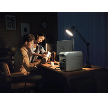 Un cuplu lucrează la un birou cu o stație de alimentare EcoFlow, un computer și o lampă de birou.