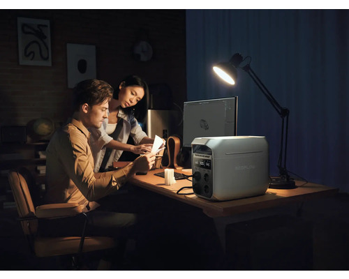 Un cuplu lucrează la un birou cu o stație de alimentare EcoFlow, un computer și o lampă de birou.