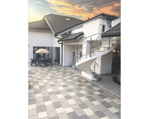 Exteriorul unei case cu pavaj, scară spiralată și zonă de relaxare sub o umbrelă de soare.