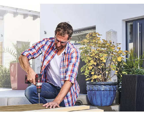 Un bărbat găurește o scândură cu o mașină de găurit cu acumulator afară.