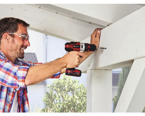 Un bărbat găurește o grindă de lemn cu o șurubelniță electrică cu acumulator.