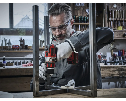 Meșter care găurește cu o mașină de găurit cu acumulator un cadru metalic într-un atelier.