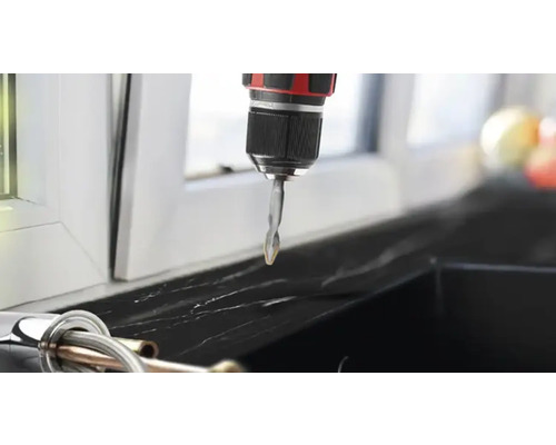 Mașină de găurit cu acumulator cu atașament de burghiu în fața unei ferestre.