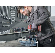 Un bărbat găurește o bucată de metal fixată într-o menghină cu o mașină de găurit cu acumulator Einhell.