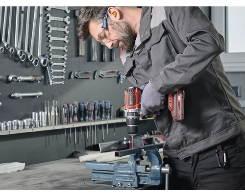 Un bărbat găurește o bucată de metal fixată într-o menghină cu o mașină de găurit cu acumulator Einhell.