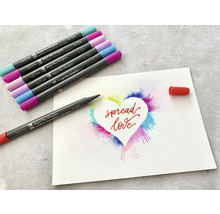 Markere acuarelă cu o ilustrație a unei inimi cu inscripția „Spread Love” (Răspândește dragoste).