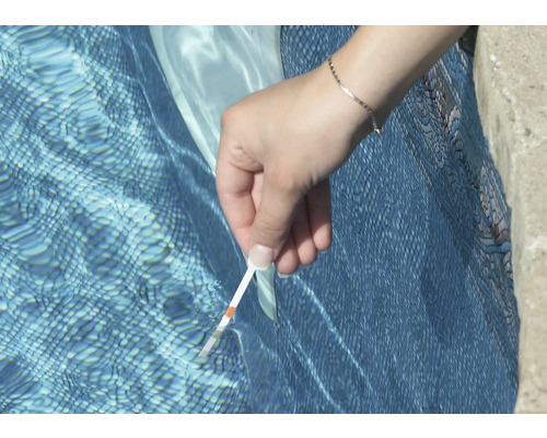 O persoană testează apa din piscină cu o bandă de testare