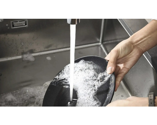 O persoană spală o tigaie într-o chiuvetă sub jet de apă.