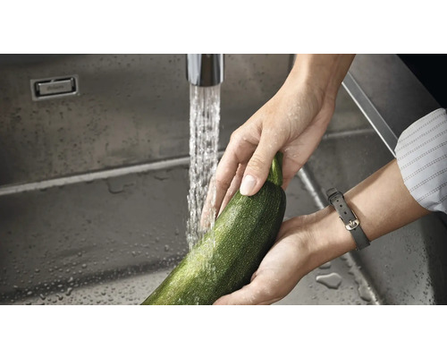 O persoană spală un dovlecel într-o chiuvetă din oțel inoxidabil sub un robinet.