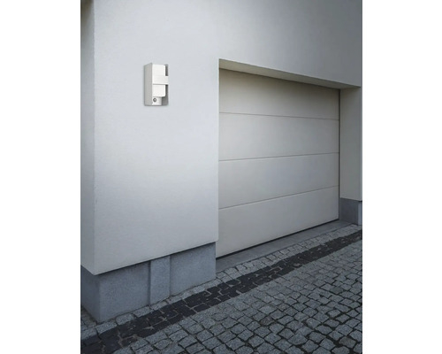 Lampă de perete metalică pentru exterior pe un perete de casă lângă un garaj