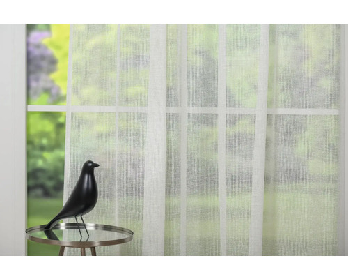 Scenă cu o perdea albă transparentă în fața unei ferestre și o figurină decorativă pe o masă