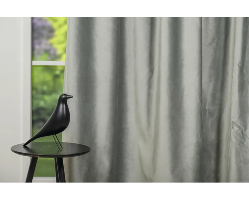 Obiect decorativ în formă de pasăre pe o masă în fața unei ferestre cu perdele.