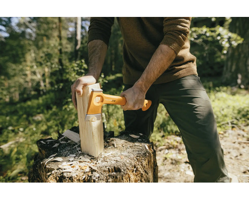 Un bărbat taie lemne cu un topor Fiskars pe un butuc de copac