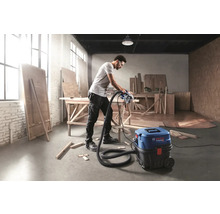 Un bărbat taie o scândură cu un ferăstrău circular conectat la un aspirator Bosch într-un atelier.