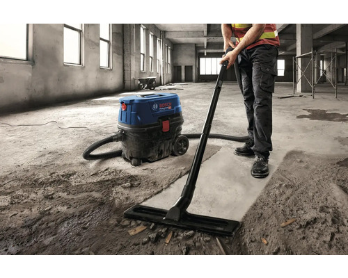 Artizan care curăță un șantier cu un aspirator industrial Bosch.