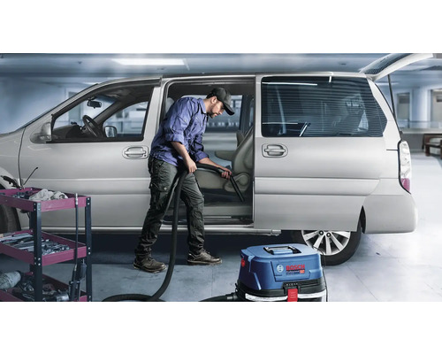 Un bărbat curăță interiorul unei mașini cu un aspirator Bosch Professional.
