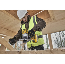 Un muncitor în construcții găurește o scândură de lemn cu o mașină de găurit fără fir DeWalt galbenă.
