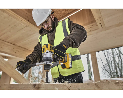 Un muncitor în construcții găurește o scândură de lemn cu o mașină de găurit fără fir DeWalt galbenă.