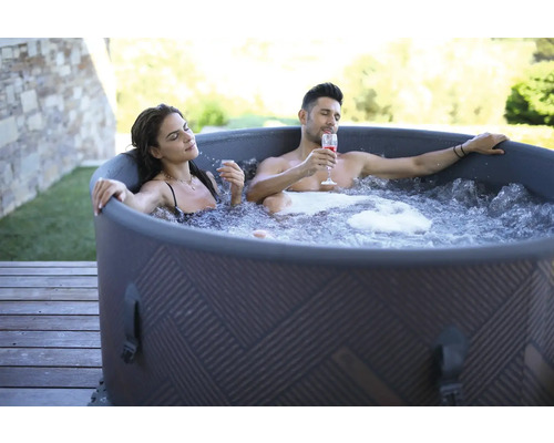 Un cuplu se relaxează într-un jacuzzi gonflabil în aer liber cu băuturi.
