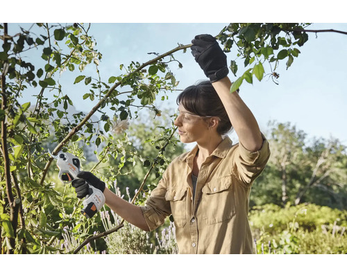 O femeie folosește un ferăstrău de grădină cu acumulator pentru a tăia crengi în grădină.