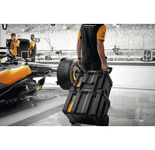 Persoană trăgând cutii de scule pe roți într-un atelier